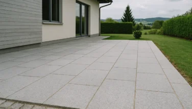 Sonnige Terrasse mit Natursteinbelag in heller Farbe neben moderner Fassade